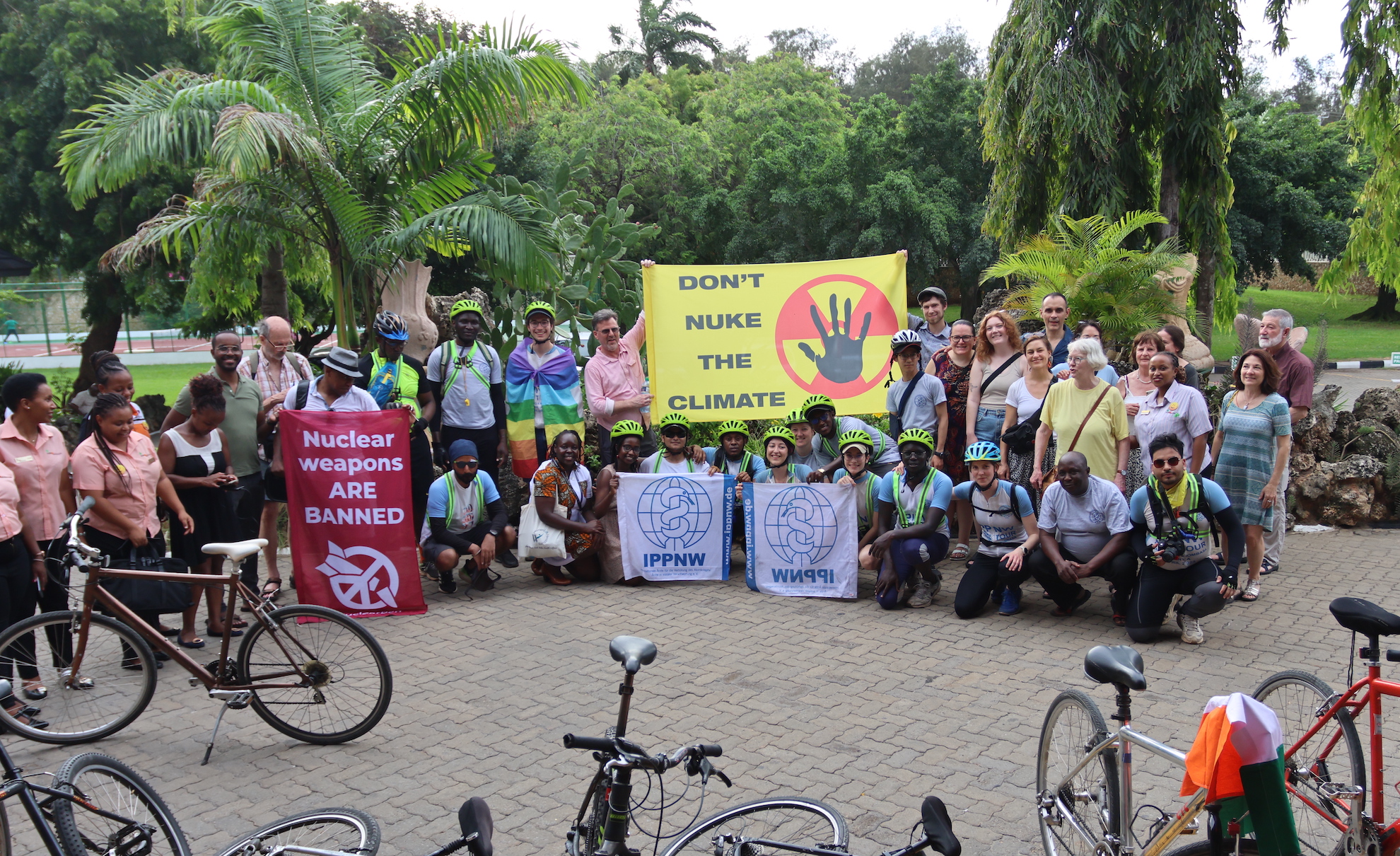 A group of people posing for a photo, most wearing cycling helmets, holding banners that say "Nuclear weapons are banned!", "Don't nuke the climate" and "IPPNW".