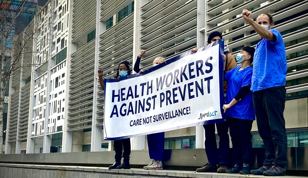 A photo of health workers protesting at the Home Office, carrying a banner ‘Health Workers Against Prevent’ banner