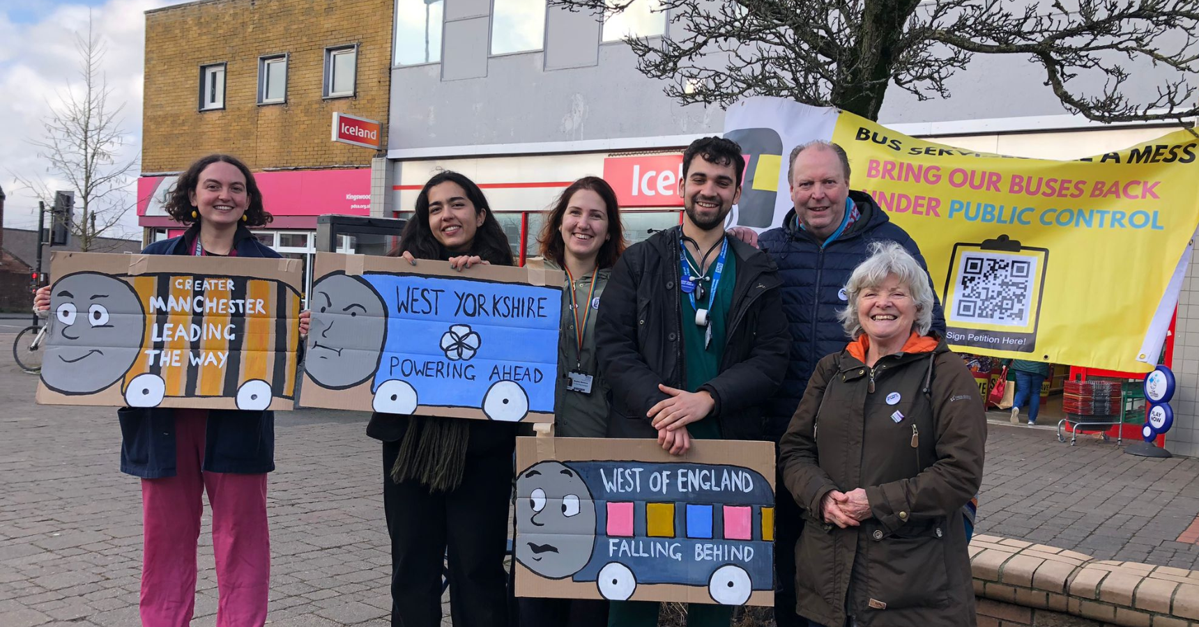 Medact Bristol health workers and local campaigners smiling at the camera in a group photo. They hold three placards with cartoon trains that read: "Greater Manchester leading the way", "West Yorkshire powering ahead", "West of England falling behind"