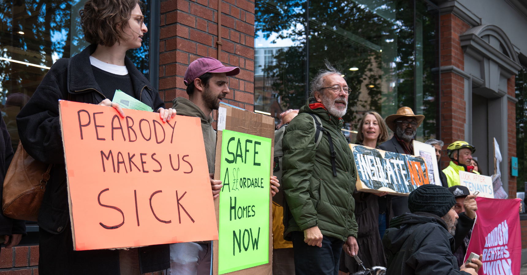 Tenants and campaigners protest at Peabody HQ in London, lined up in front of the building, holding placards that read 'Peabody Makes us Sick', and 'Safe Affordable Homes Now'. (Photo: TJ Chuah / Medact)