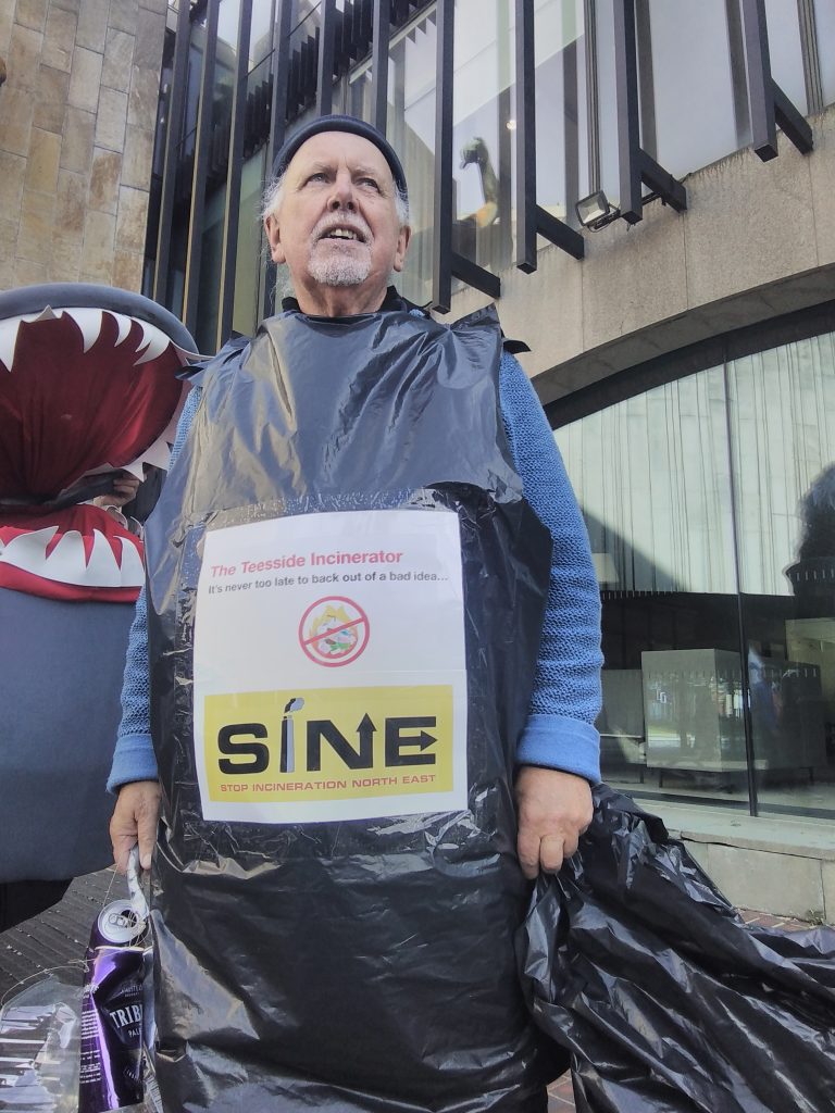 A man wearing a bin-bag costume with a big sign on the front reading 'The Teesside Incinerator: It's never too late to back out of a bad idea.