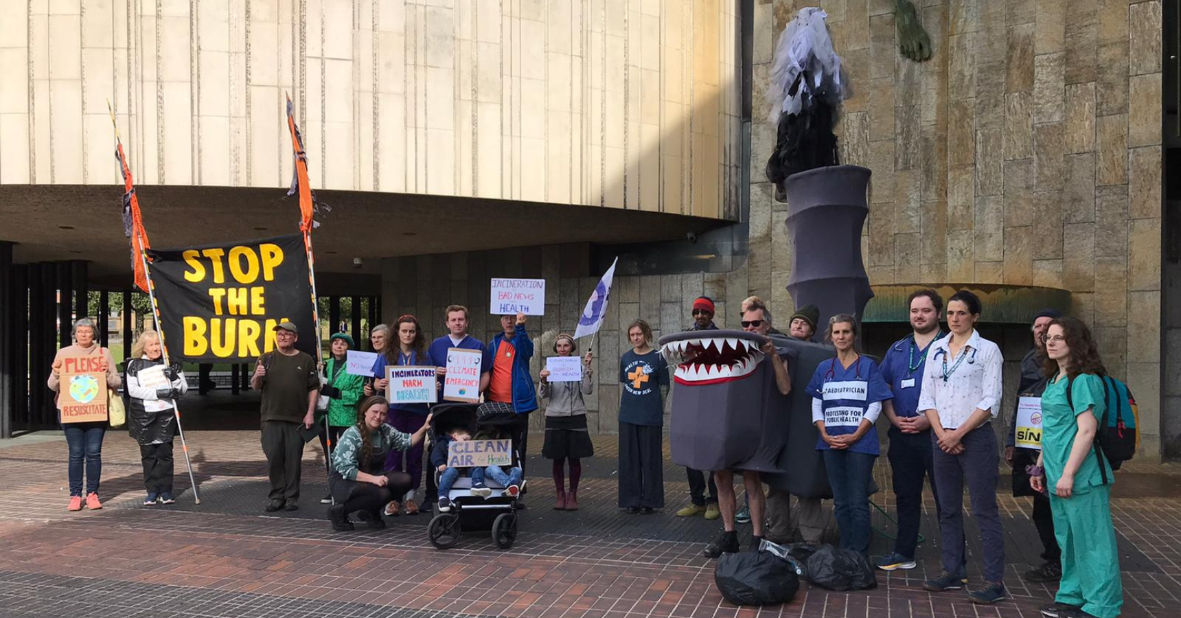 Protestors including Health workers in a row outside Newcastle Civi Centre, holding signs like "Clean Air for Health", and "Incinerators Harm Health", as well as a huge banner saying "Stop The Burn"