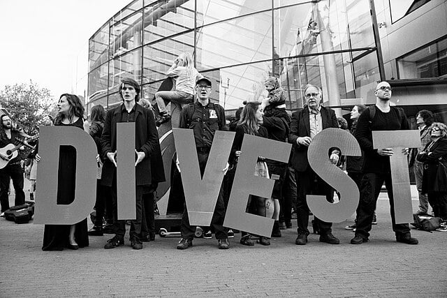 Black and white photo of campaigners lined up each holding a giant letter spelling out 'DIVEST'