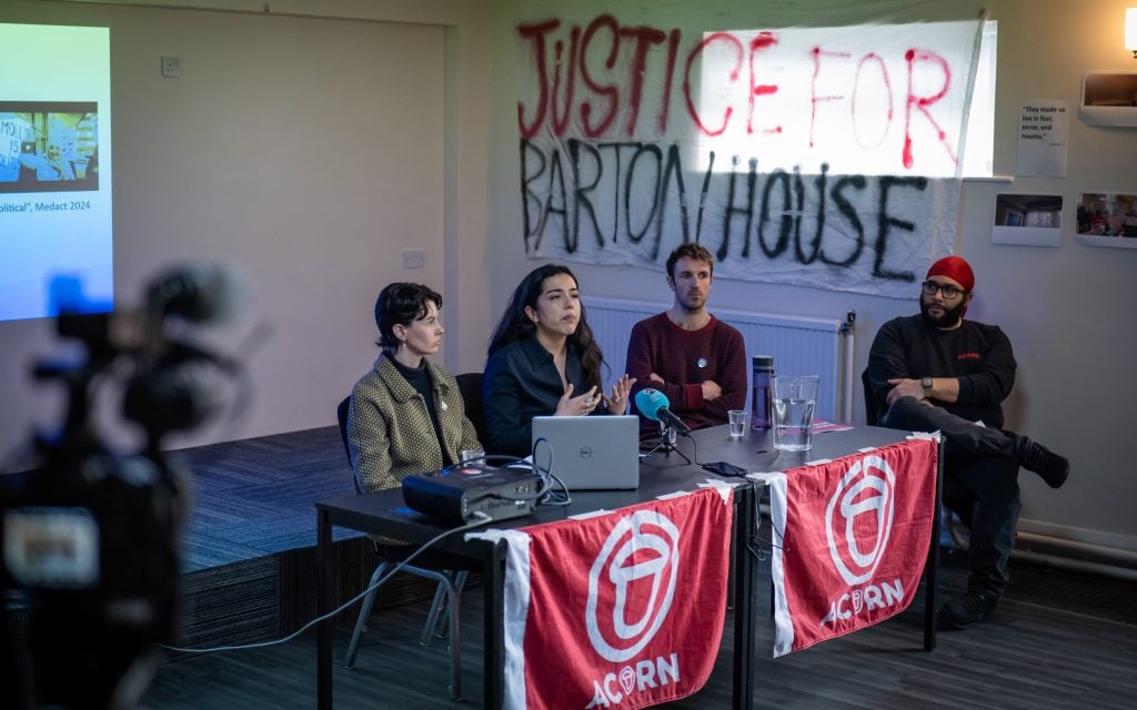 Medact Bristol members Naz, Amelia and Francis, and ACORN Bristol's Wesley, present the report in front from a stage in front of a large 'Justice for Barton House' banner