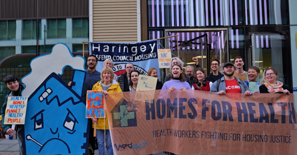 Campaigners protesting outside the Department for Health and Social Care behind a big blue unhappy house model and a large 'Homes for Health' banner