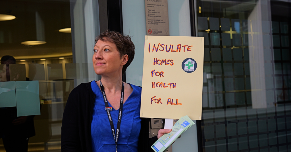 A white woman in doctor uniform holding "Insulate homes for health for all" placard